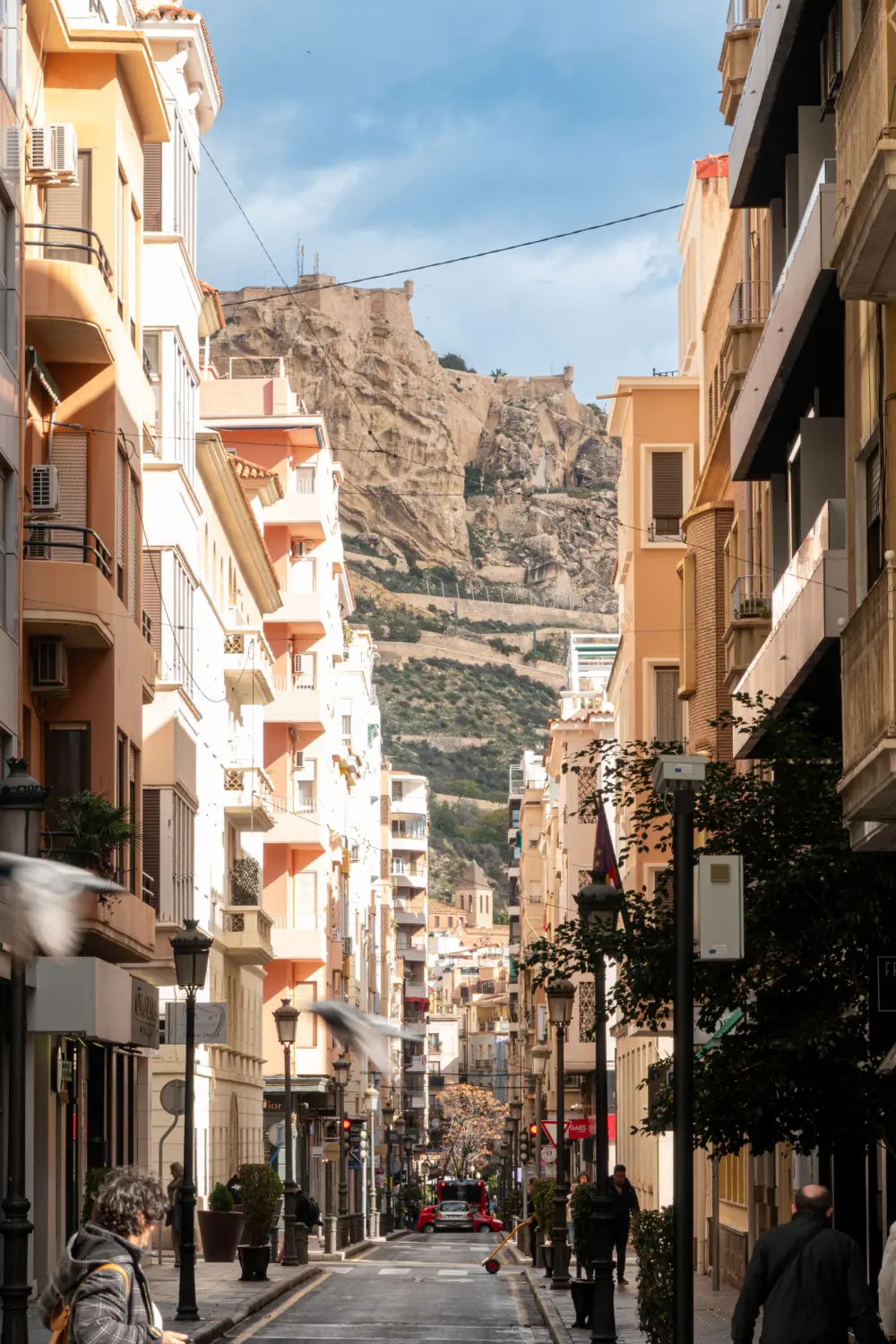 Calle del centro de Alicante en un día soleado con el castillo de Santa Bárbara al fondo